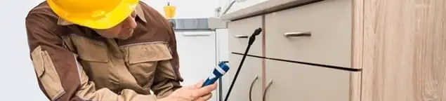 Roach exterminator applying treatment under kitchen cabinets in St Paul, MN