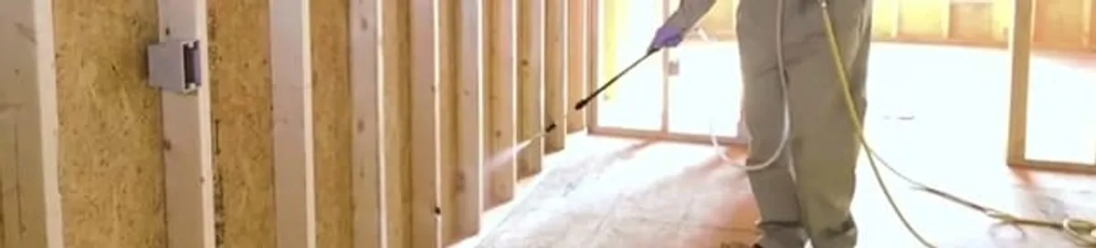 Termite treatment technician applying spray along framing and unfinished walls in St Paul, MN