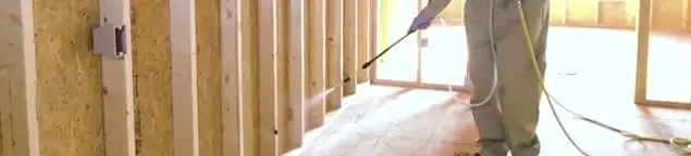 Termite treatment technician applying spray along framing and unfinished walls in St Paul, MN
